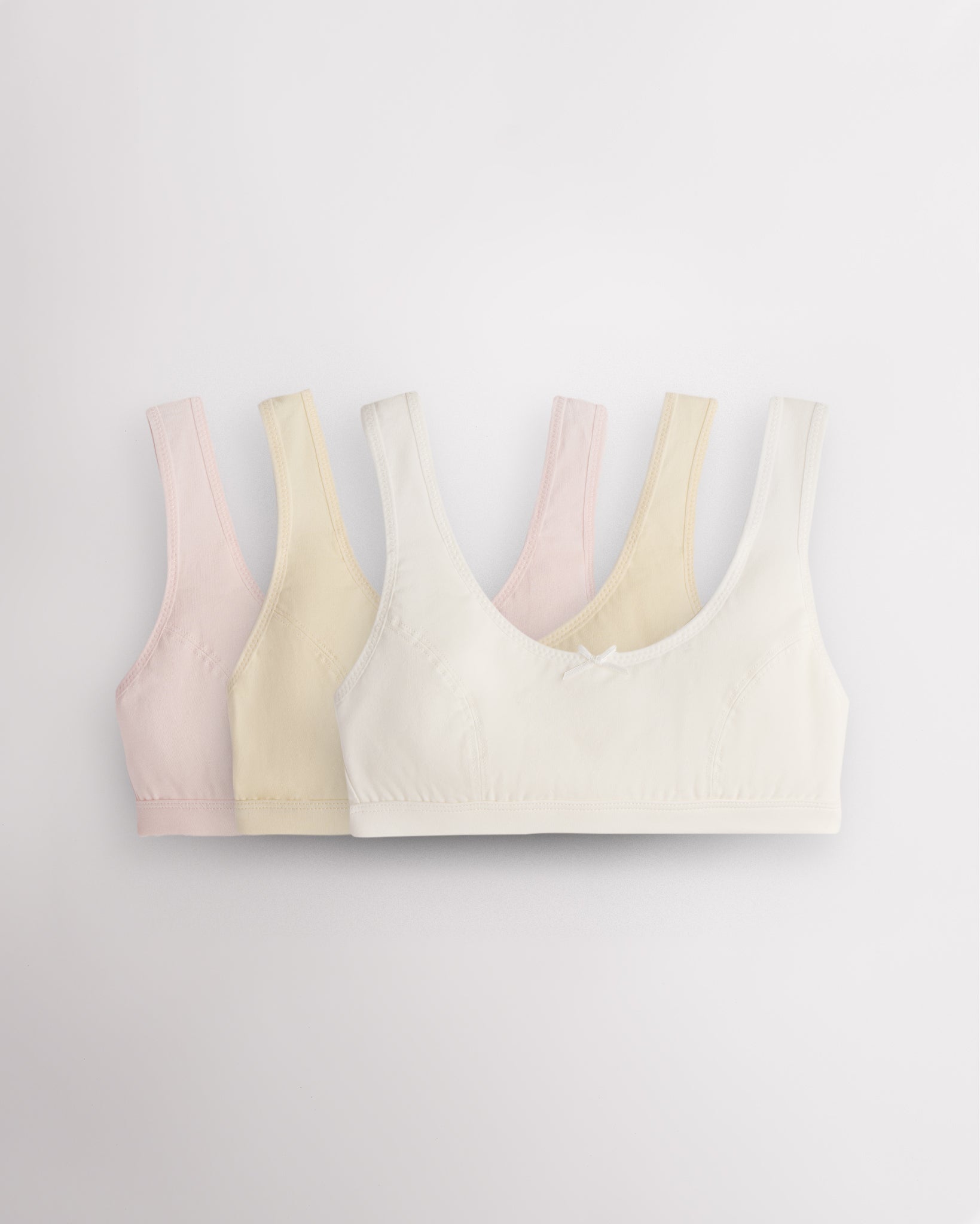 Three Stelle girls cotton bralettes in white, soft butter, and whisper pink with wide straps and bow details