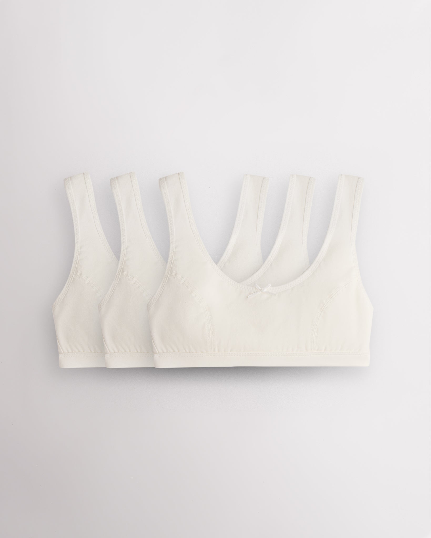 Three Stelle girls cotton bralettes in white with wide straps, soft lining, and small bow detail.