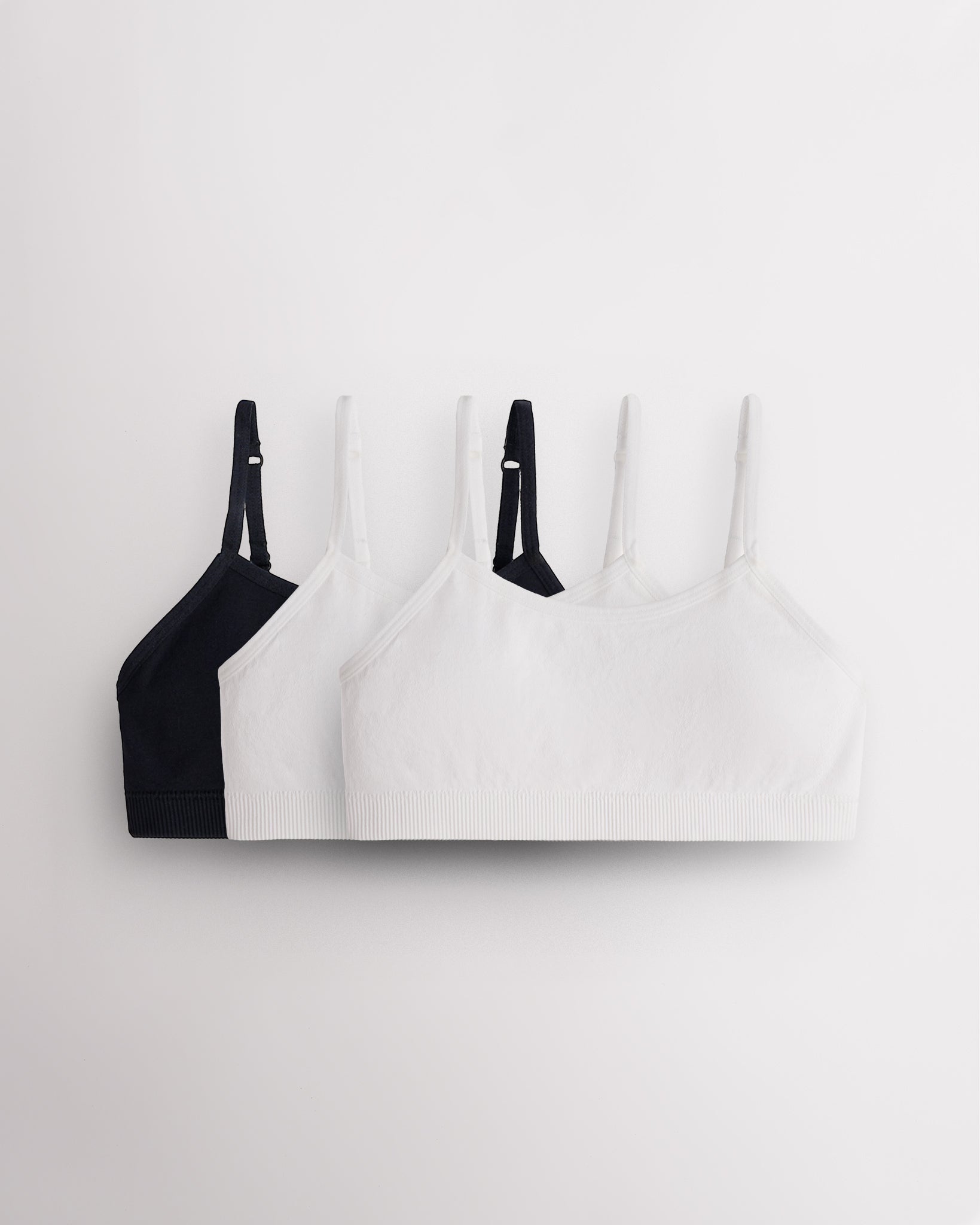 Three Stelle girls seamless cami bras in black and white with slim adjustable straps and soft ribbed bands.