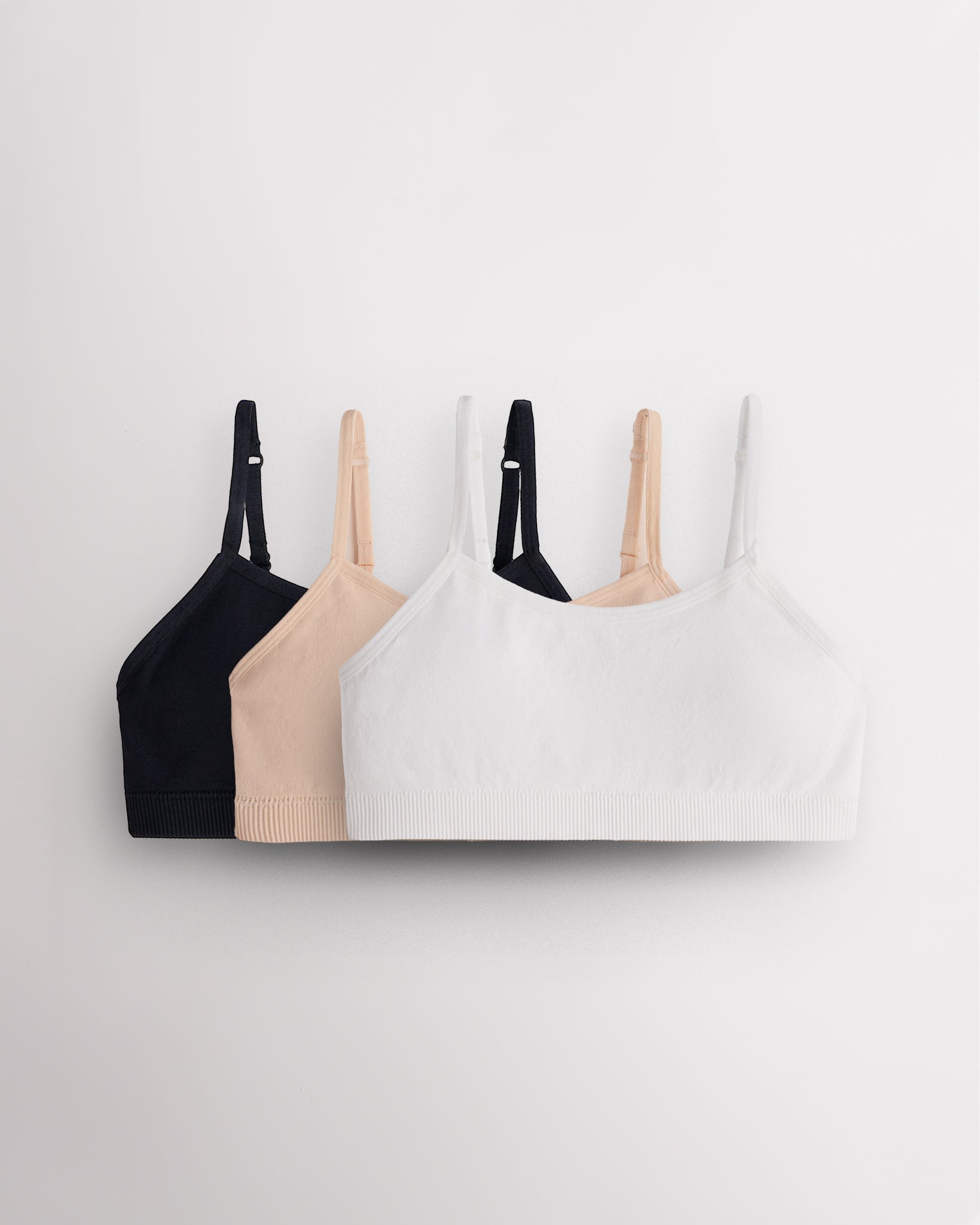 Three Stelle girls seamless cami bras in black, Soft Butter and white with slim adjustable straps and soft ribbed bands.