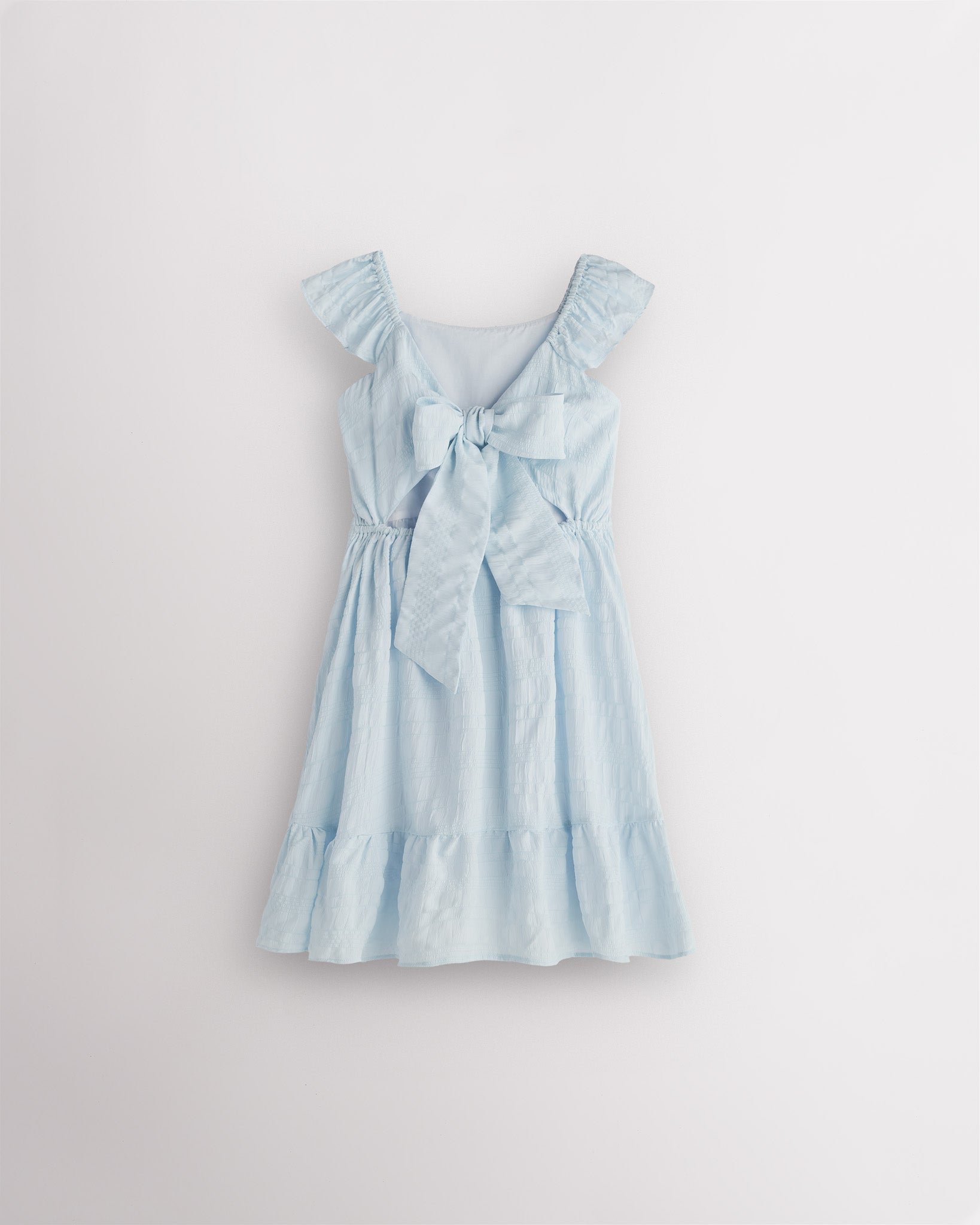 Girls light blue flutter sleeve sundress with adjustable bow back, smocked waist, and tiered skirt, back view showing bow detail