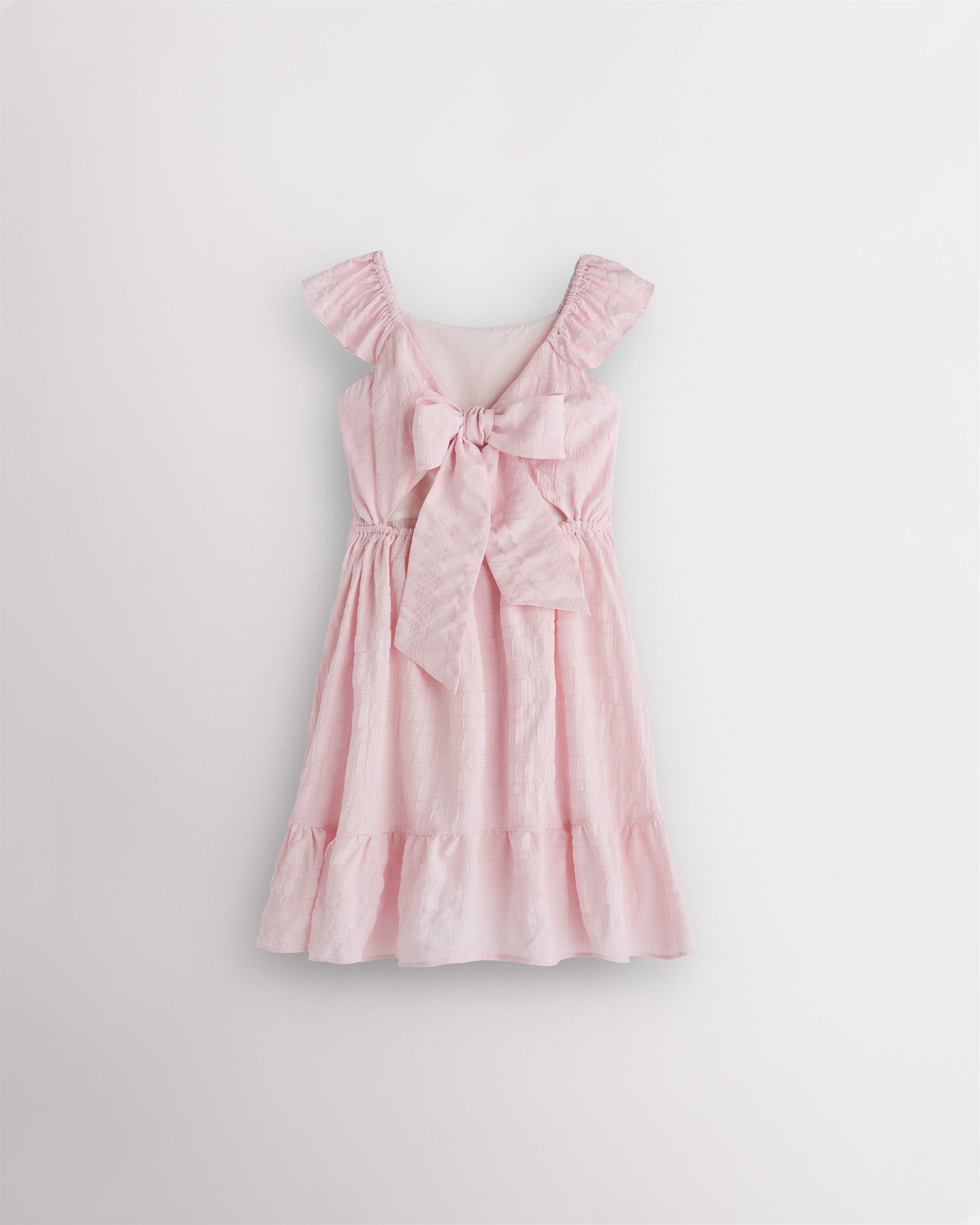 Girls light pink flutter sleeve sundress with adjustable bow back, smocked waist, and tiered skirt, back view showing bow detail