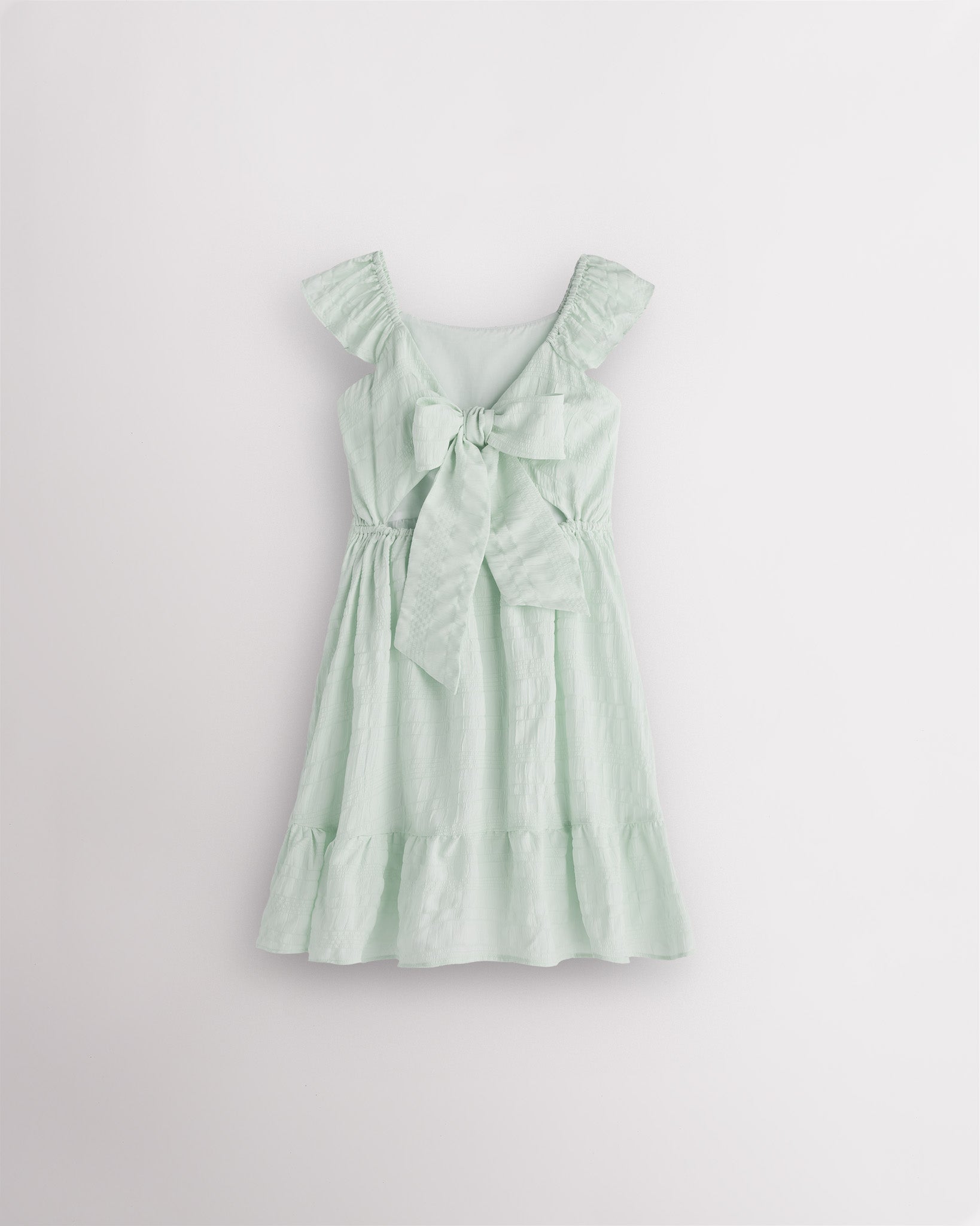 Girls pastel green flutter sleeve sundress with adjustable bow back, smocked waist, and tiered skirt, back view showing bow detail