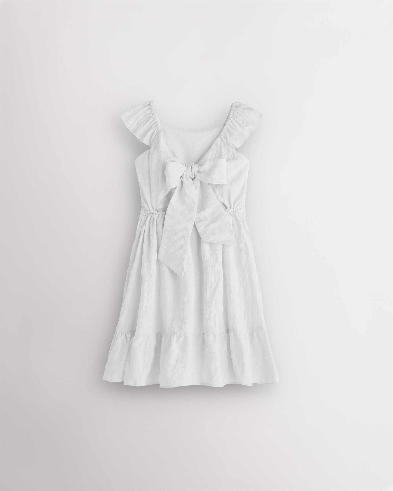 Girls white flutter sleeve sundress with adjustable bow back, smocked waist, and tiered skirt, back view showing bow detail