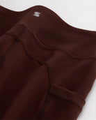 Close-up of coffee girls flare leggings showing soft 4-way stretch fabric, waistband seam, side pocket detail, and small Stelle logo.