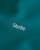 Close-up of the embroidered Stelle logo on the teal fleece hoodie.
