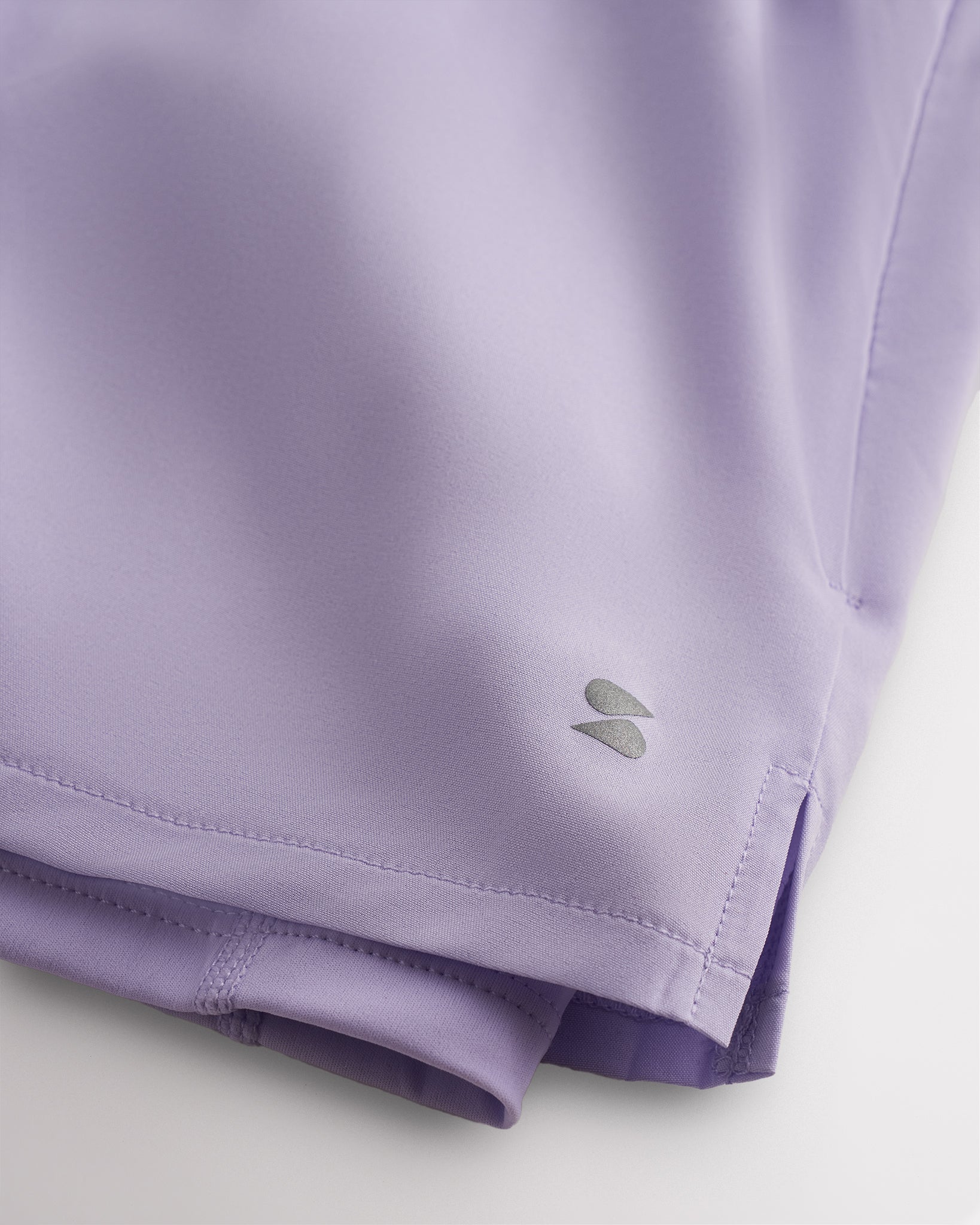 Close-up of lavender Stelle running shorts showing smooth fabric, subtle side slit, inner shorts liner, and logo detail.