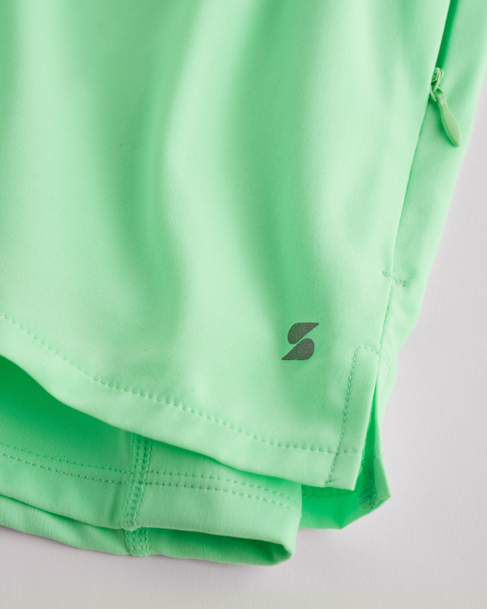 Close-up of Neon Green Stelle running shorts showing smooth fabric, subtle side slit, inner shorts liner, and logo detail.