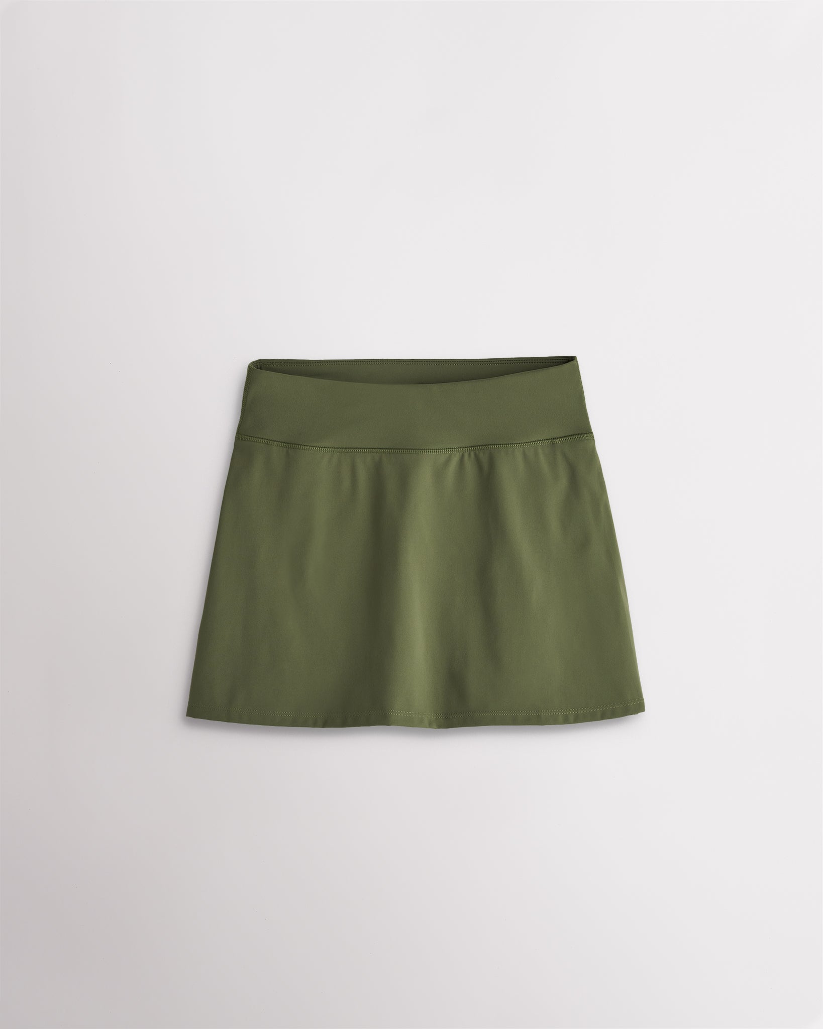 A quick-dry army green tennis skirt with a smooth front, ruffle back hem, and built-in shorts with pockets for comfortable coverage on and off the court.