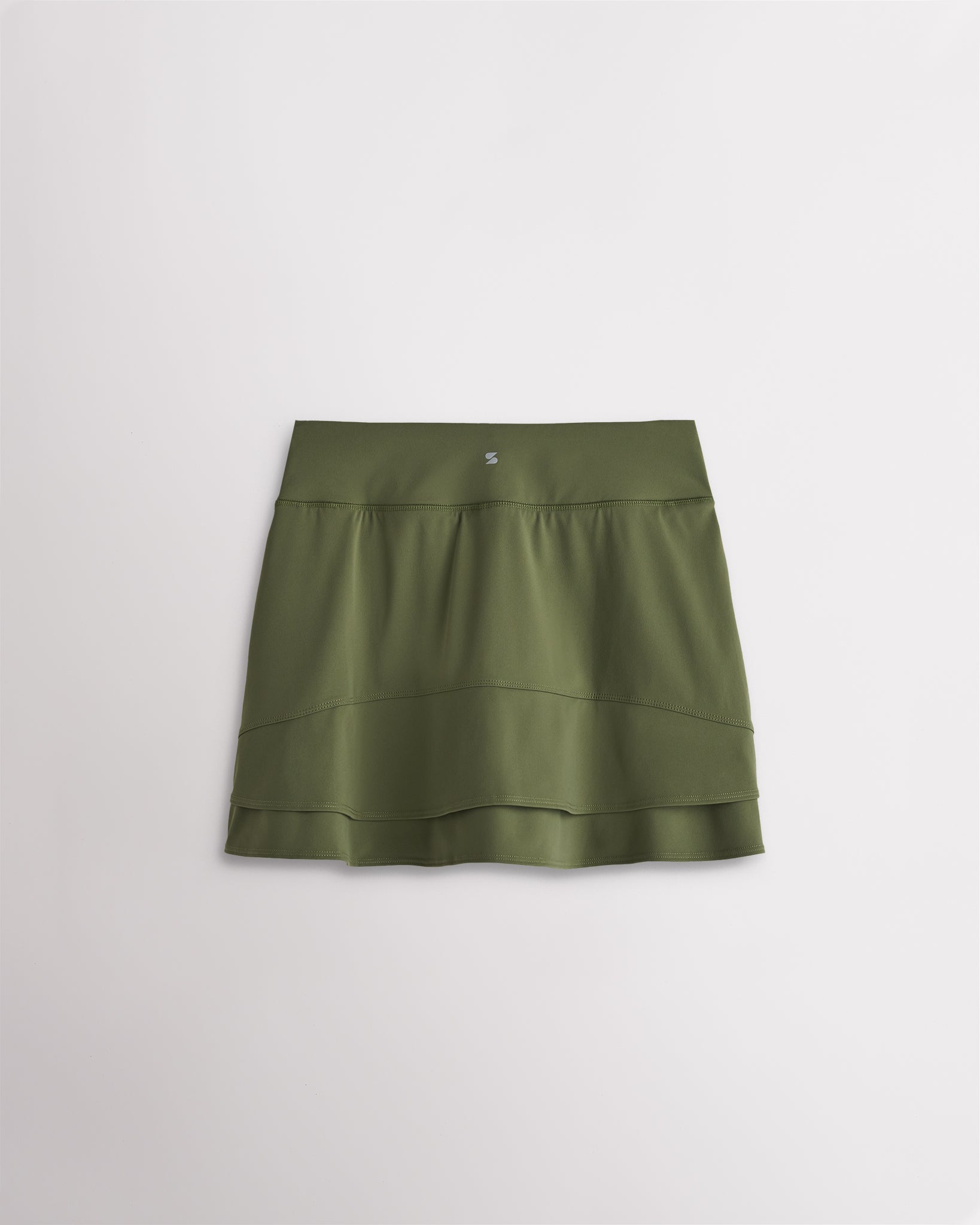 A quick-dry army green tennis skirt with a smooth front, ruffle back hem, and built-in shorts with pockets for comfortable coverage on and off the court.