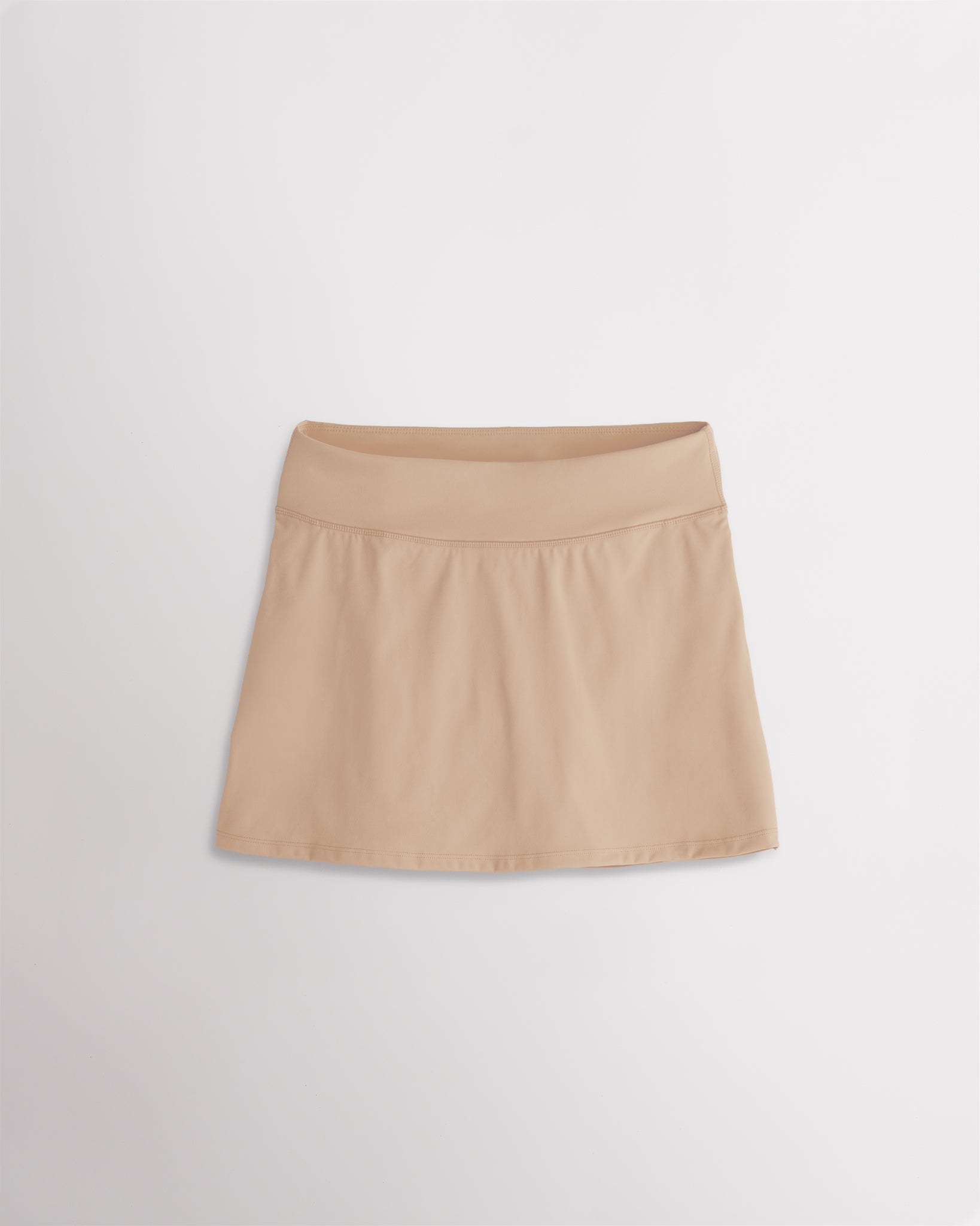 A quick-dry khaki tennis skirt with a smooth front, ruffle back hem, and built-in shorts with pockets for comfortable coverage on and off the court.