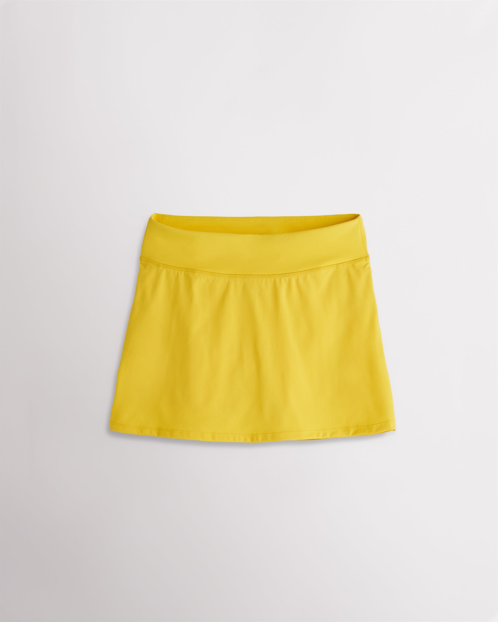 A quick-dry yellow tennis skirt with a smooth front, ruffle back hem, and built-in shorts with pockets for comfortable coverage on and off the court.