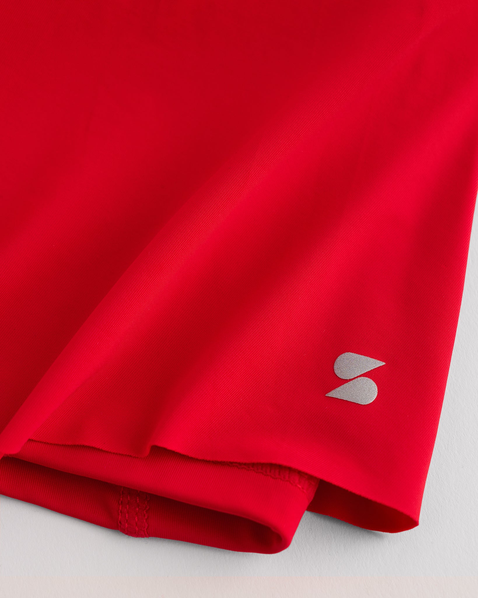 Close-up of red Kids Let’s Bounce Shorts showing lightweight quick-dry fabric, hem stitching, and small Stelle logo detail.