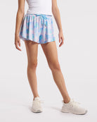 Girl wearing Watercolor Bloom 2-in-1 flowy shorts with a drawstring waist, white tank top, and white sneakers.