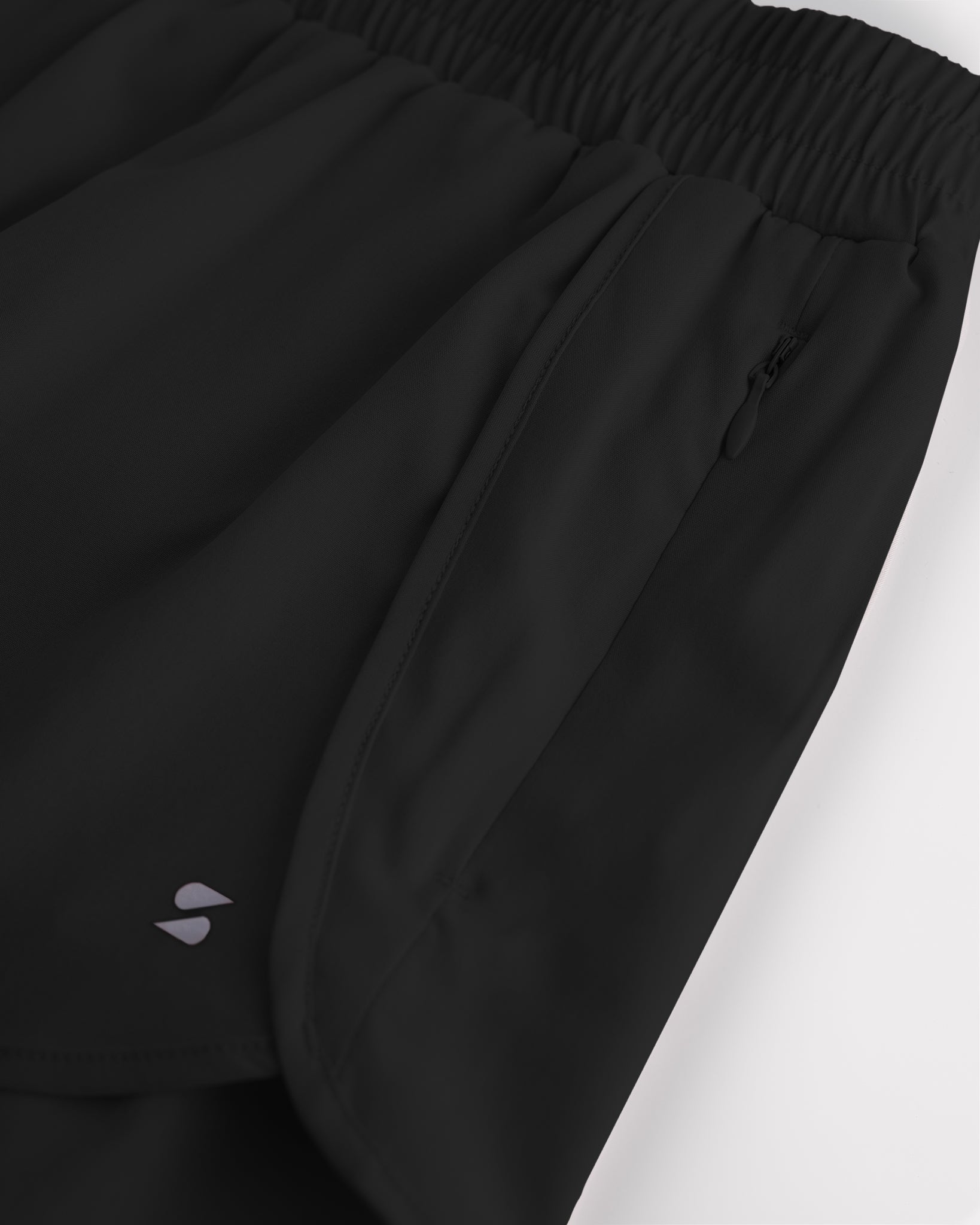 Close-up of girls black running shorts showing elastic waistband, curved seam, and zipper pocket detail.