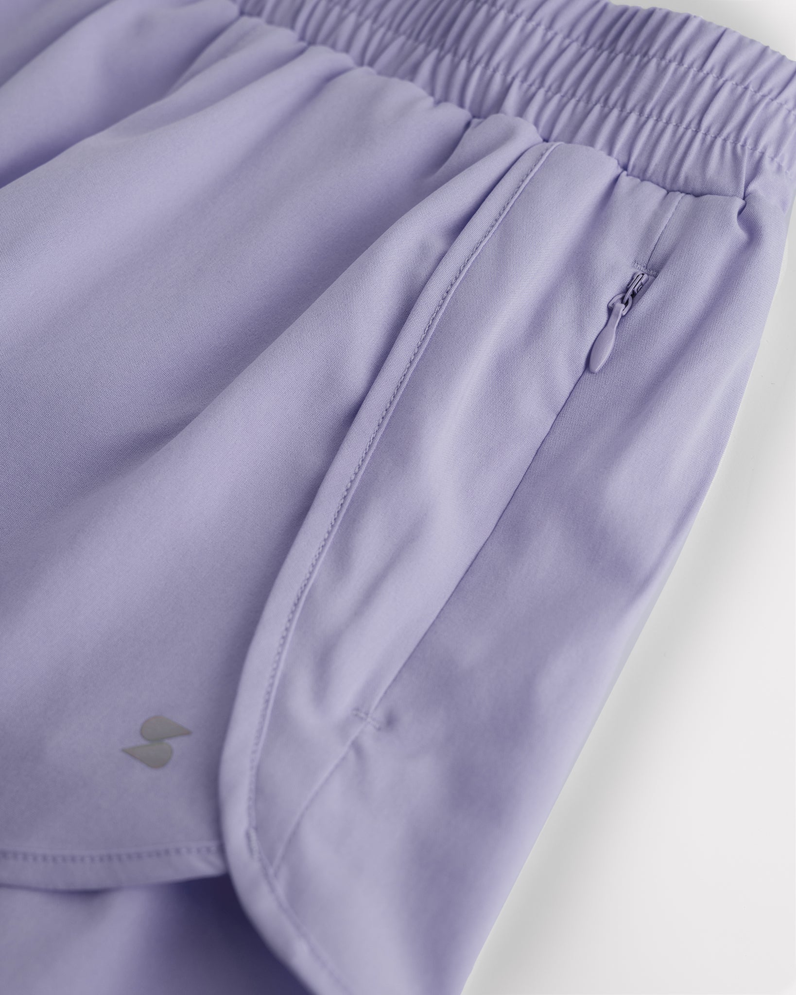 Close-up of girls purple haze running shorts showing elastic waistband, curved seam, and zipper pocket detail.