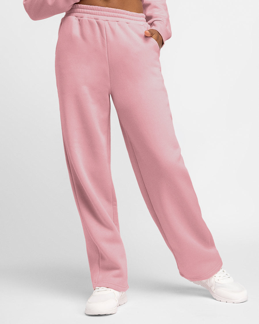 Front view of girl wearing pink kids fleece sweatpants with roomy pockets, straight-leg silhouette, and white sneakers.