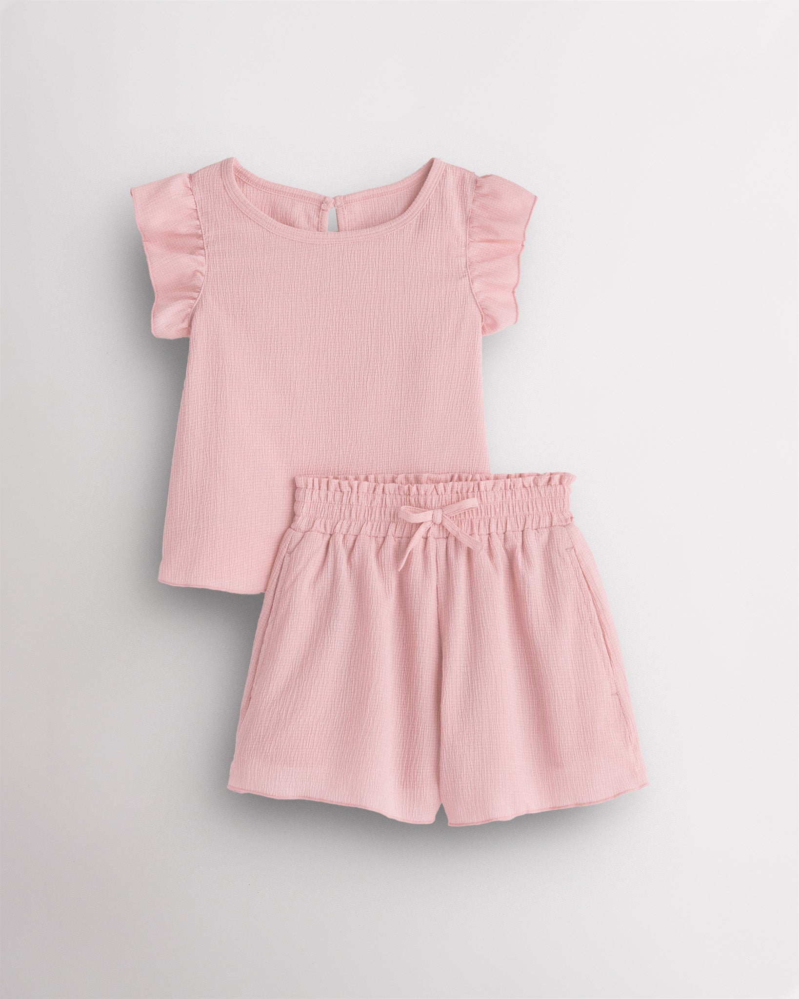 Girls blush pink flutter sleeve summer outfit set with textured top, button-back detail, and matching elastic waist shorts with bow.