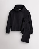 Black Stelle kids waffle knit lounge set with a hooded top and matching pants, laid flat on a grey background.