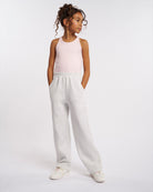 Girl wearing Stelle Fleece Out Kids Sweatpants in Light Heather Grey with a pale pink ribbed tank top, hands in pockets, front view