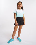 Girl wearing Stelle kids ombre athletic t-shirt with black shorts and aqua sneakers