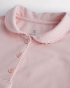 Close-up of a girls light pink pique polo shirt showing the Peter Pan collar, scalloped trim, and front button placket.