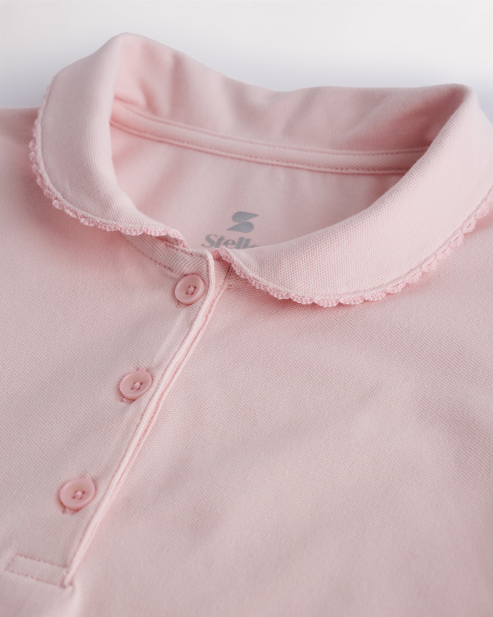 Close-up of a girls light pink pique polo shirt showing the Peter Pan collar, scalloped trim, and front button placket.