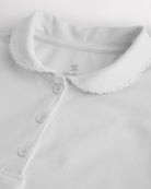 Close-up of a girls white pique polo shirt showing the Peter Pan collar, scalloped trim, and front button placket.
