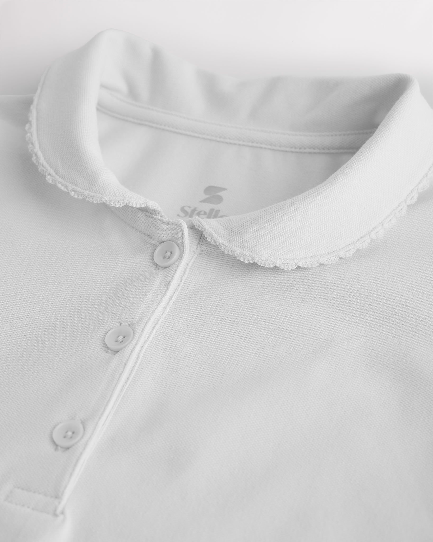 Close-up of a girls white pique polo shirt showing the Peter Pan collar, scalloped trim, and front button placket.