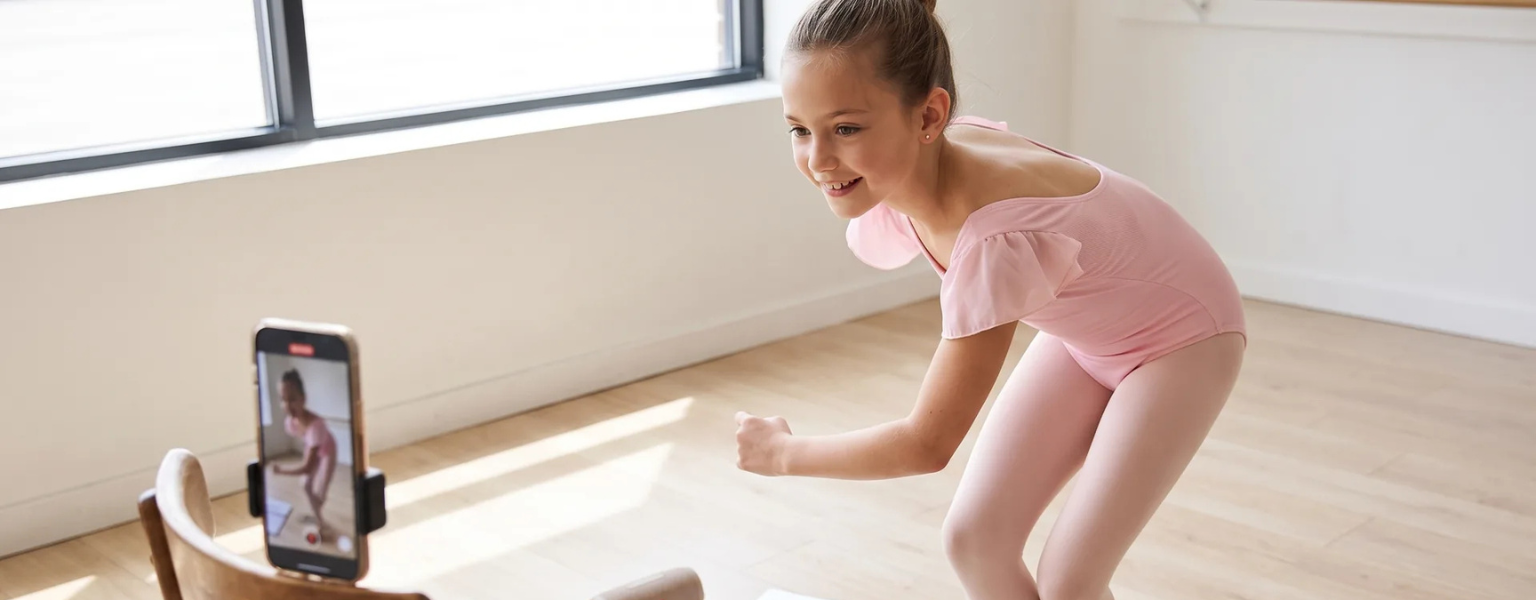 Young dancer marking out choreography counts in a bright studio with phone and notebook nearby
