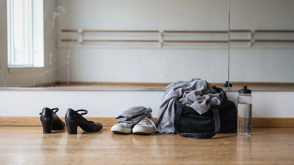 Block heel dance shoes, knee pads, and sneakers set out on a studio floor, showing what to wear to a heels dance class