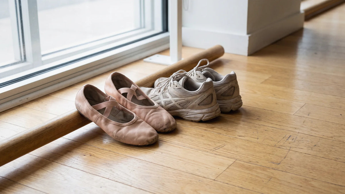 Worn pink ballet shoes next to athletic sneakers on a studio floor, asking whether ballet is a sport