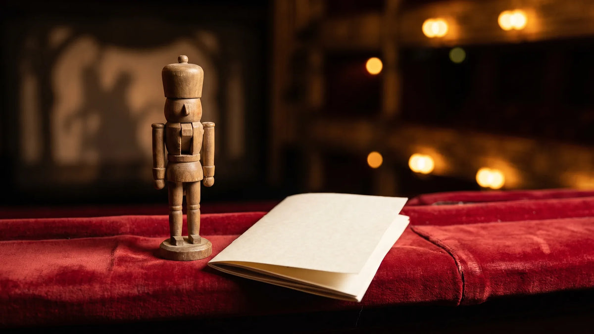 Wooden nutcracker doll on a red velvet theater seat beside a program