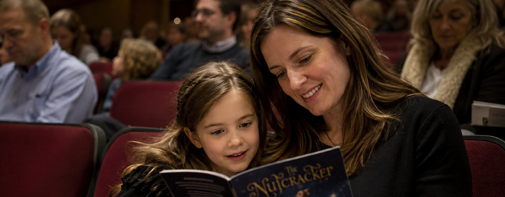 Child and parent sitting in a theater before a ballet performance, reading a Nutcracker program together.