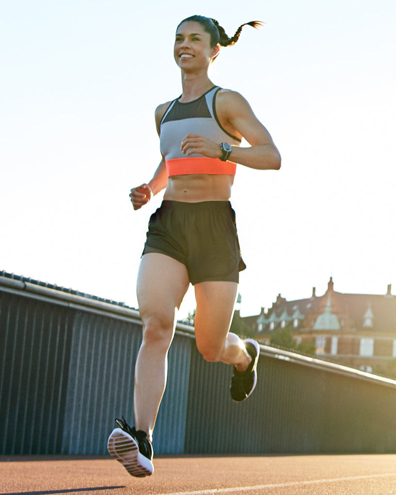 Smiling woman running outdoors in running shorts at sunset