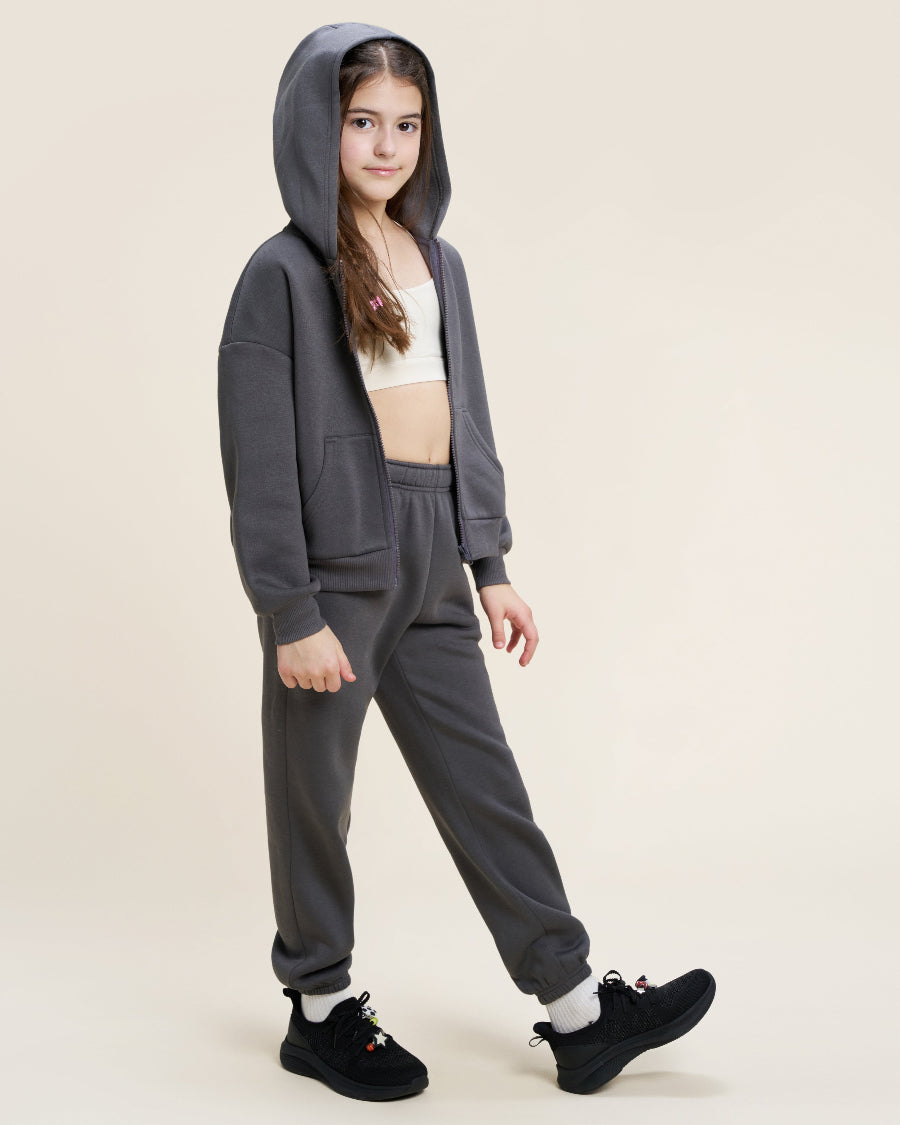 Person wearing a gray hoodie and matching pants on a beige background