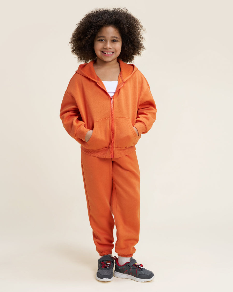 Child wearing an orange tracksuit on a beige background