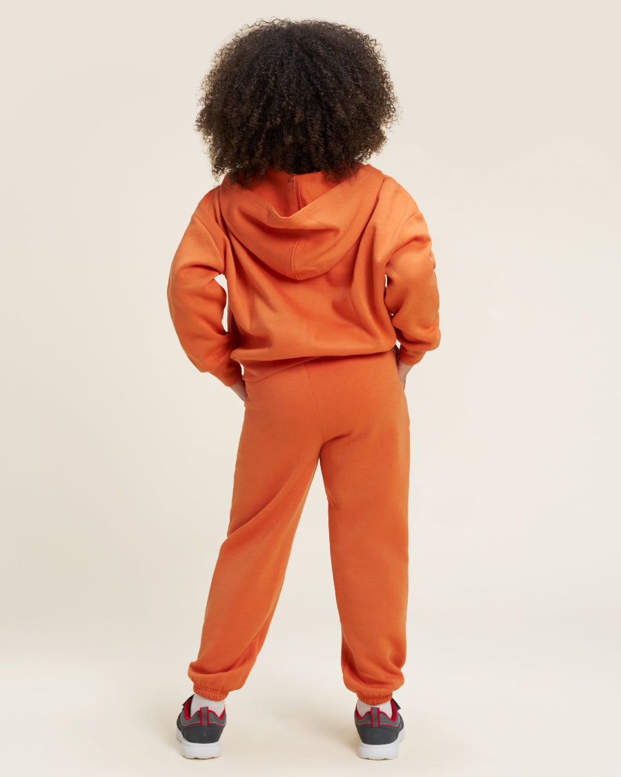Person wearing an orange tracksuit on a beige background