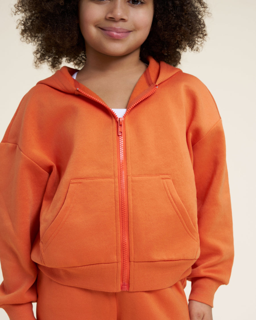 Child wearing an orange hoodie and pants on a beige background