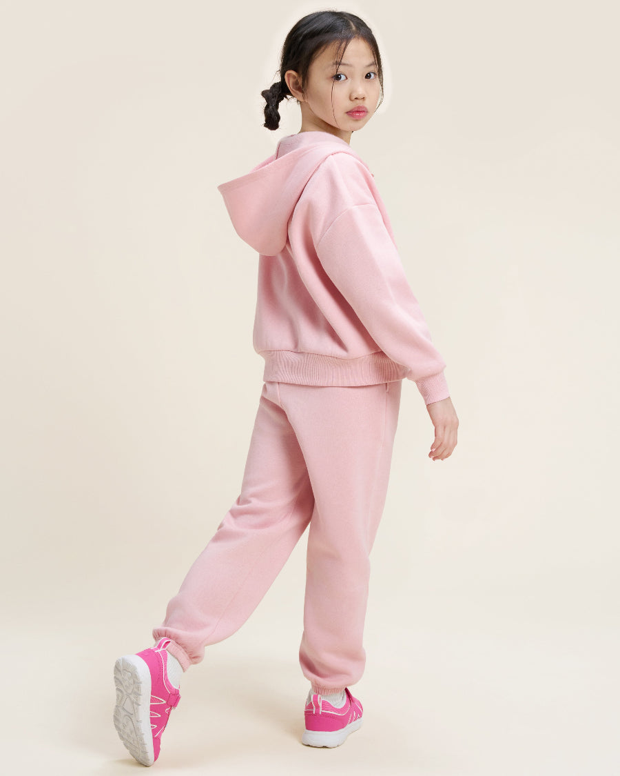 Child wearing a pink tracksuit on a beige background