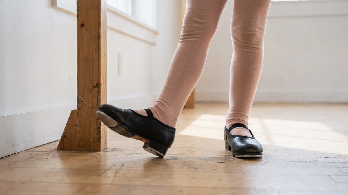 Time steps in tap dance start with basics: a child practicing a shuffle at the barre in a naturally lit studio
