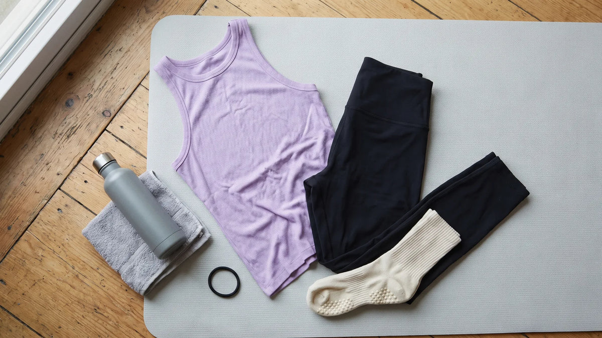 First Pilates class essentials laid out on a mat: fitted tank, leggings, grip socks, water bottle and hair tie